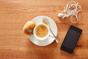 Having coffee and croissants with smartphone and headphones